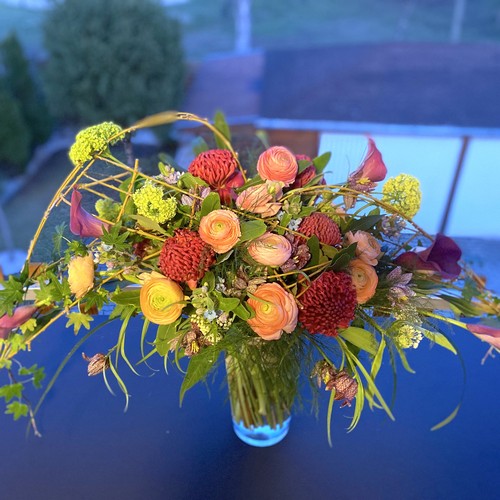Orange ranunculus red chrysanthemums and calla lilies in a glass vase at dusk for luxury flower delivery Durham